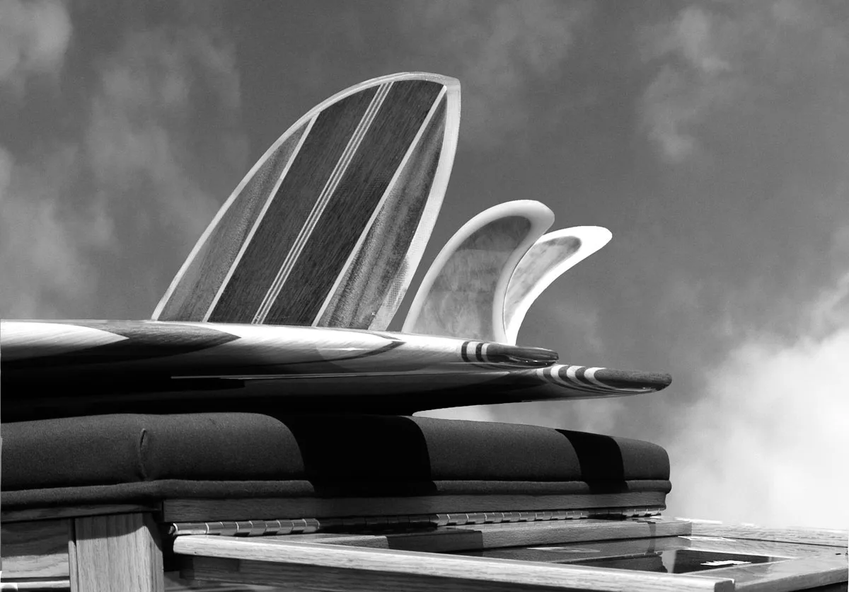 Wood-finned boards stacked on a surf wagon roof, fins silhouetted against the sky