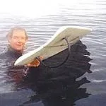 Surfer in a wetsuit floats beside his board, showing its hoop fin