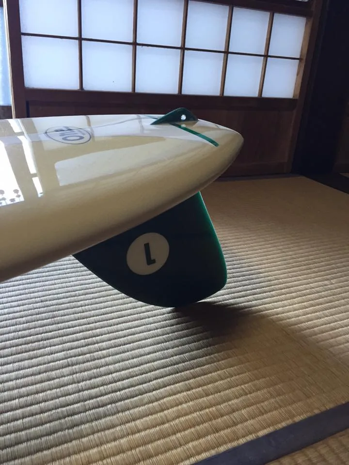 Cream longboard on a tatami mat with a dark green glassed-on single fin
